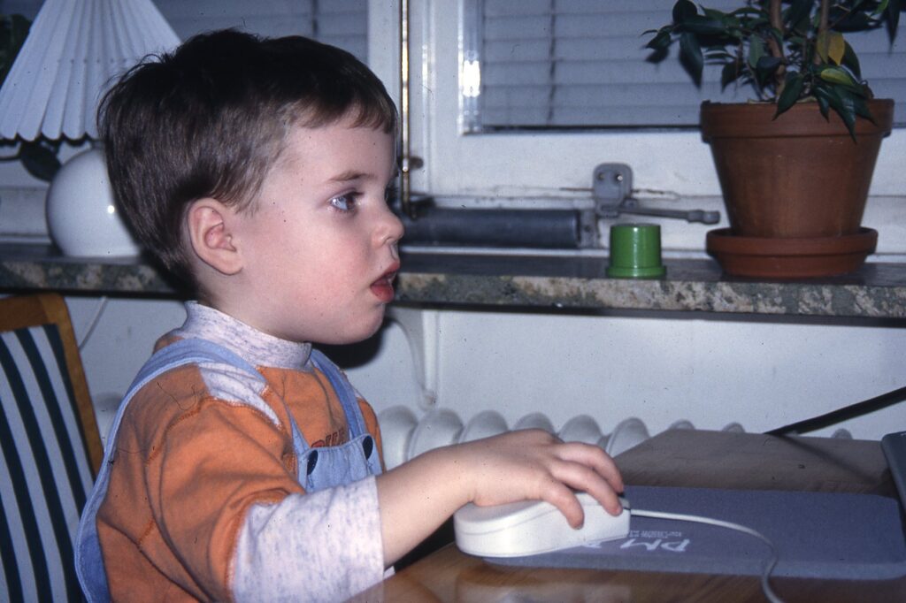 Jacob Westberg at two years old playing a game with a computer mouse, focused on the screen that's outside the frame